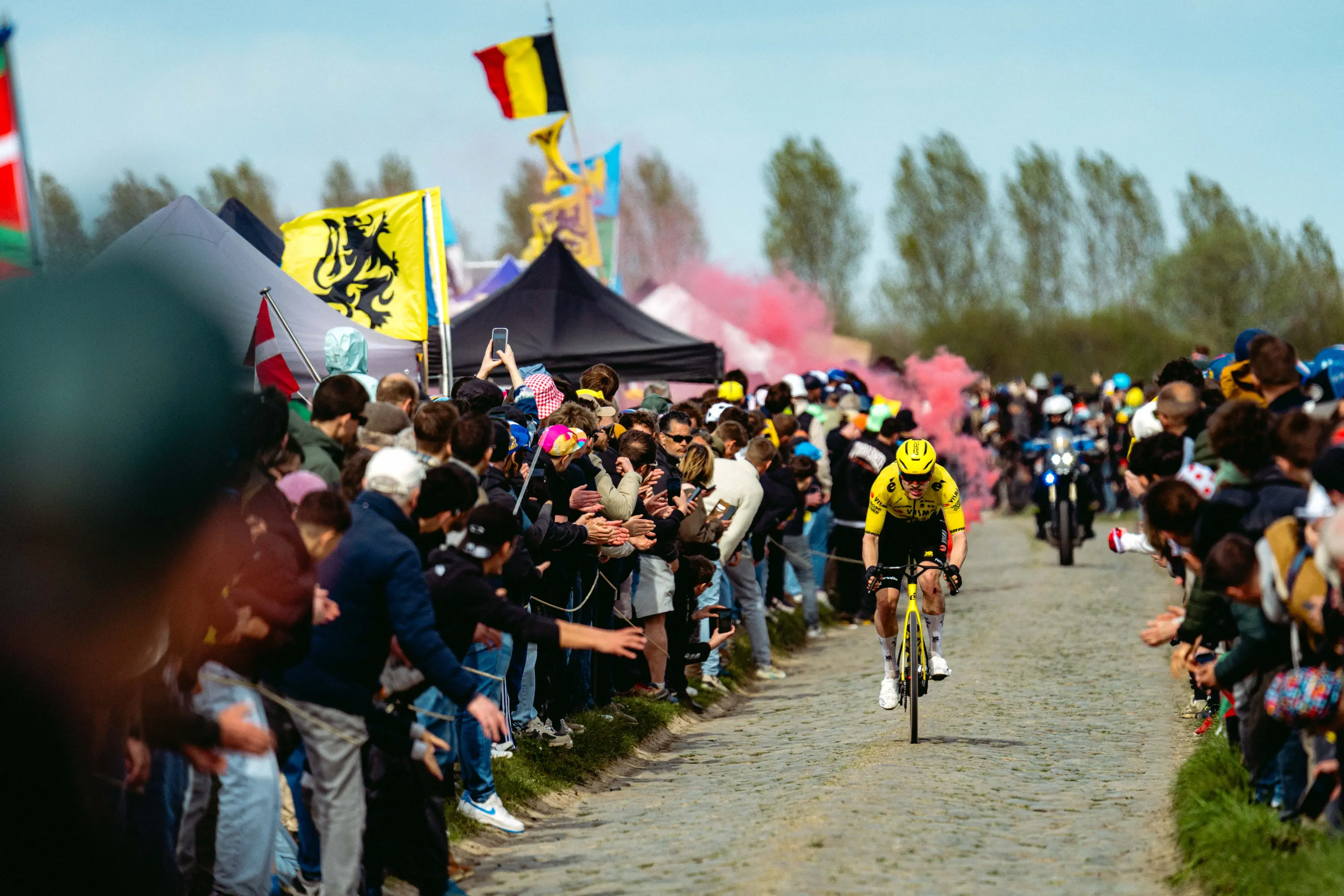 Visma rider on the pavé, with a burning bengal flare glowing in the background
