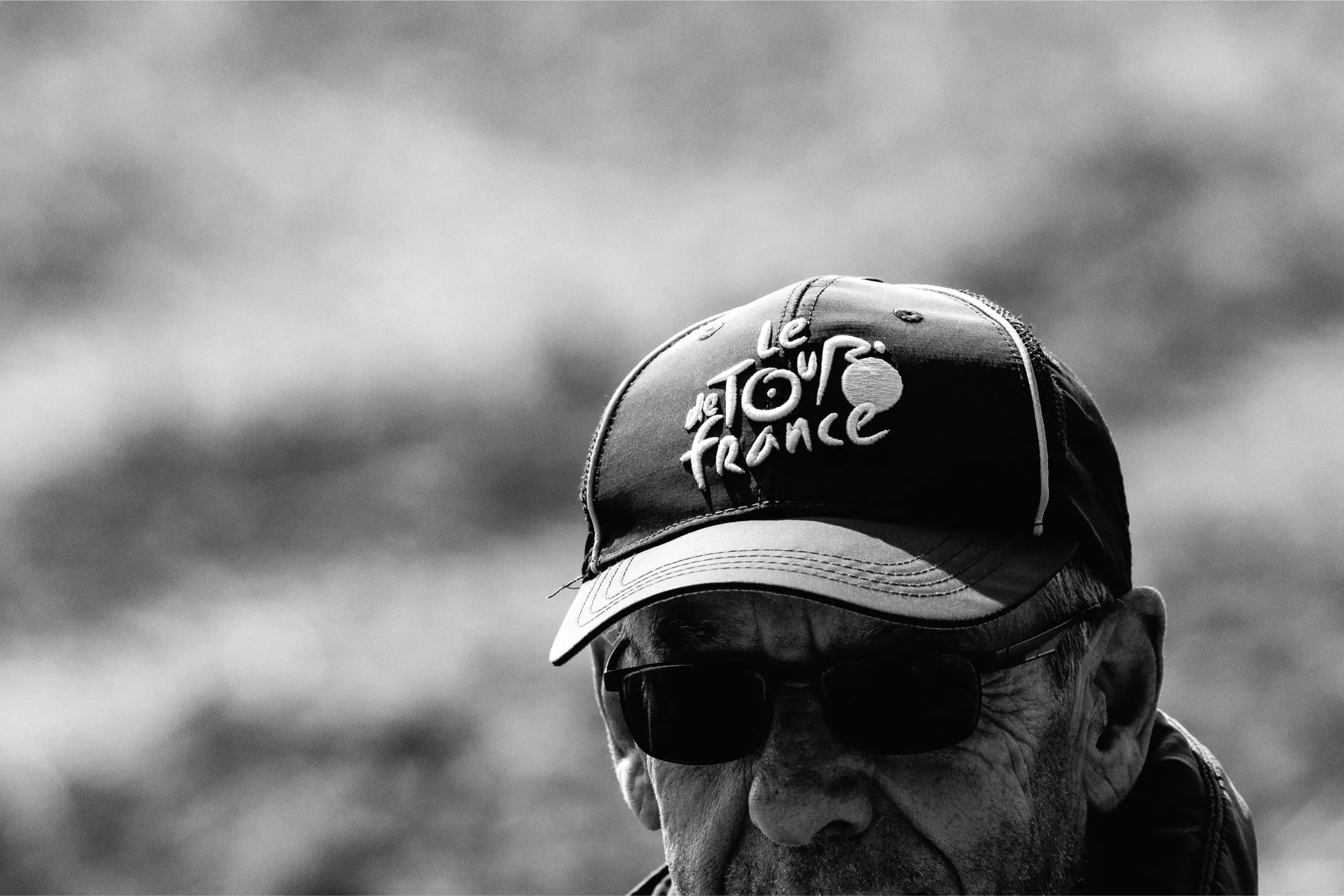 A man wearing an old Tour de France cap at the roadside