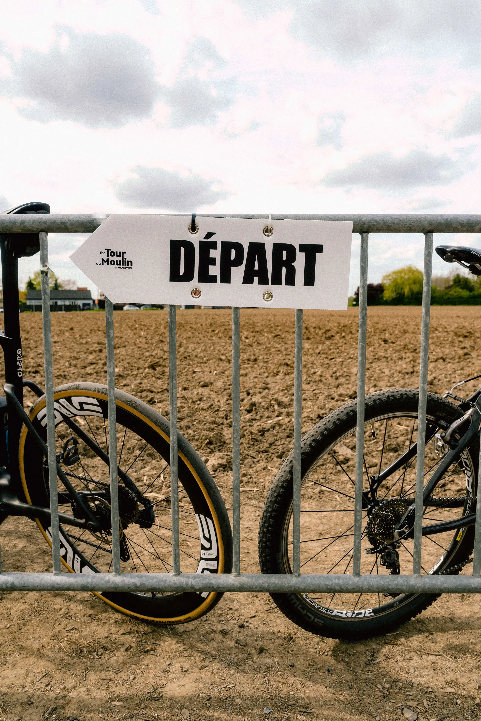 Zwei Van-Rysel-Gravelbikes an einem metallenen Absperrgitter mit DÉPART-Schild am Sektor Moulin